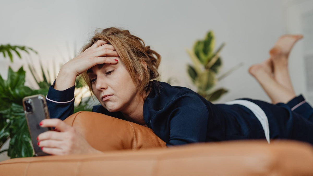 Žena leži na kauču s rukom na čelu – stres i umor